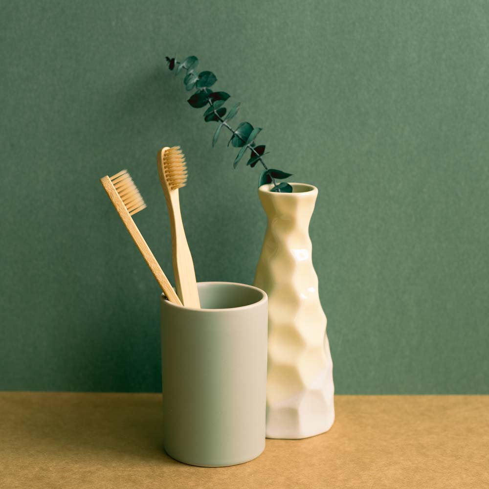 Bamboo toothbrush in a cup and eucalyptus leaf on brown shelf